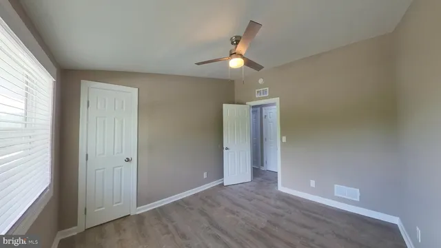 an empty room with wooden floor chandelier fan and windows
