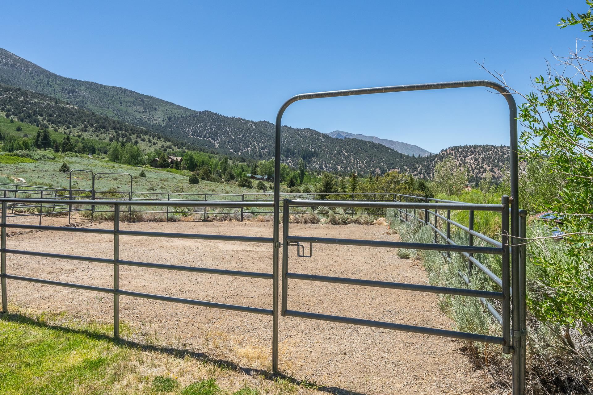 537 Aspen Spring Ranch Road Mammoth Lakes, CA 93546 - Photo 29 of 40 Gated property perimeter with metal fencing and an open corral area, surrounded by natural shrubbery and distant mountains