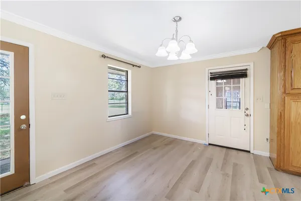 an empty room with wooden floor chandelier and windows
