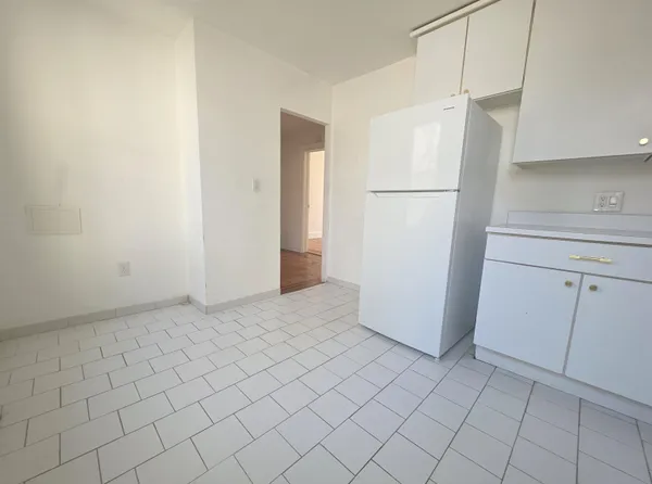 a view of a refrigerator in kitchen and an empty room with wooden floor
