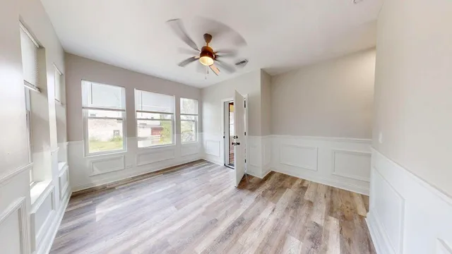 an empty room with wooden floor fan and windows