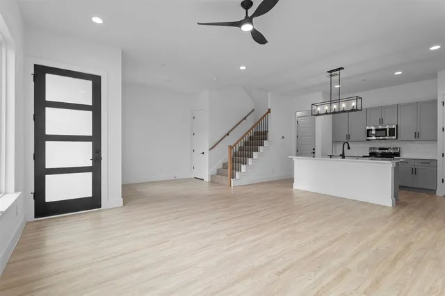 an empty room with wooden floor staircase and kitchen view