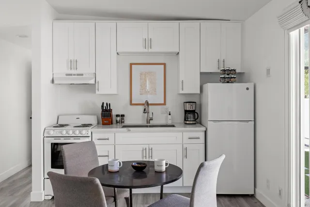 a kitchen with stainless steel appliances a white refrigerator a stove a sink and white cabinets with wooden floors