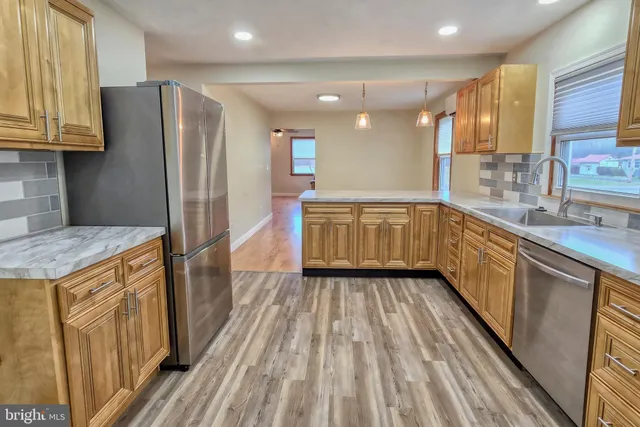 a kitchen with stainless steel appliances granite countertop a refrigerator a sink dishwasher a stove and white countertops with wooden floor