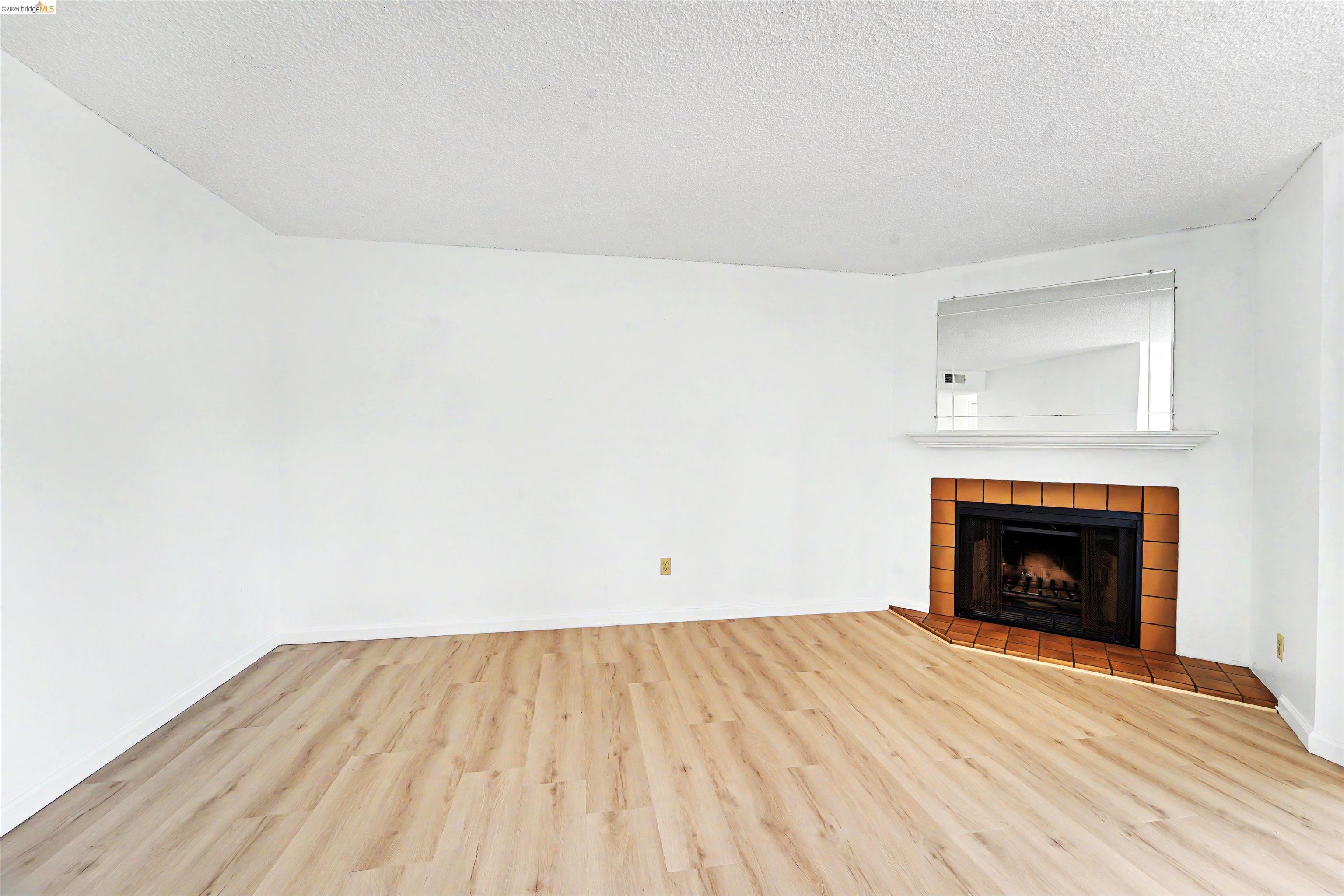 4186 San Pablo Dam Road, Unit A El Sobrante, CA 94803 - Photo 7 of 34 Living area featuring wood-finish flooring, a corner fireplace with a tile surround, a white mantel, and an integrated mirror