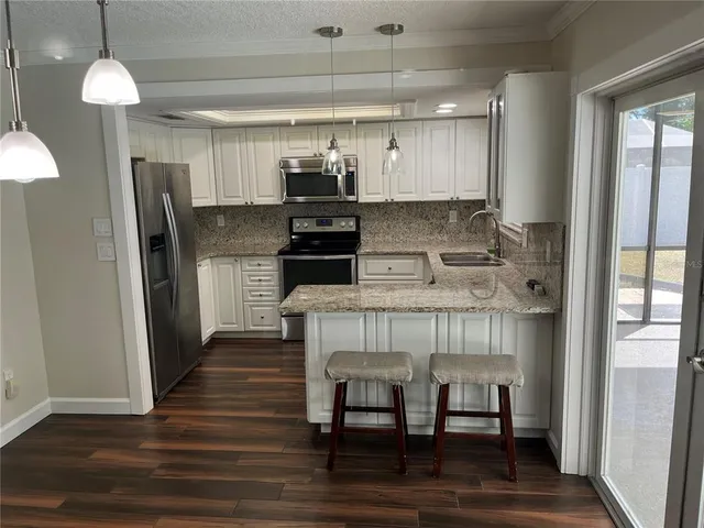 a kitchen with stainless steel appliances granite countertop a refrigerator a stove and a wooden floor