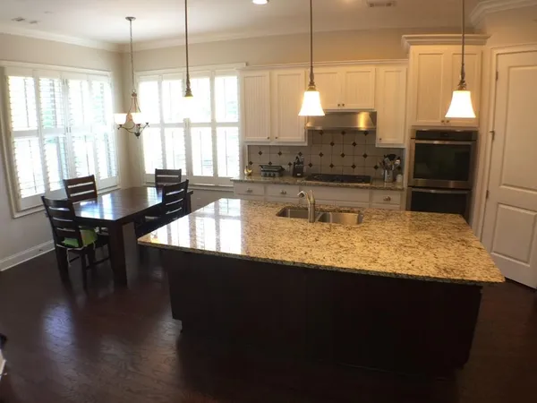 a kitchen with stainless steel appliances granite countertop a stove a refrigerator a sink a dining table and chairs with wooden floor