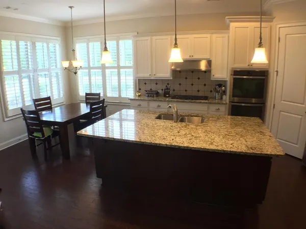 a kitchen with stainless steel appliances granite countertop a stove a sink dishwasher a refrigerator a dining table and chairs with wooden floor