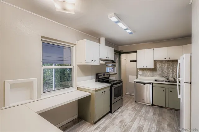 a kitchen with stainless steel appliances granite countertop a stove a sink dishwasher a refrigerator and white cabinets with wooden floor