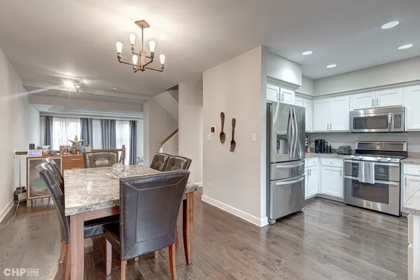 a kitchen with stainless steel appliances kitchen island granite countertop a refrigerator a stove a microwave oven a dining table and chairs with wooden floor