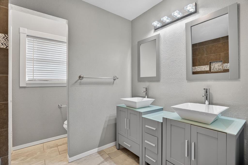 6609 Genoa Road Fort Worth, TX 76116 - Photo 25 of 40 Double vanity featuring vessel sinks with chrome faucets, gray cabinetry, and glass countertops