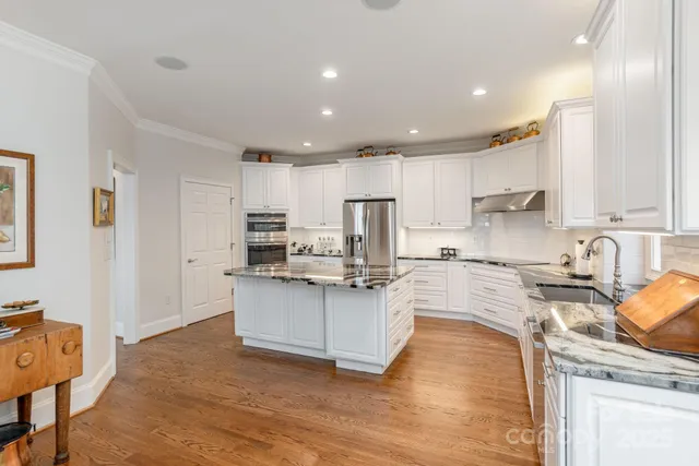 a kitchen with stainless steel appliances granite countertop a stove top oven a sink dishwasher and a refrigerator with wooden floor