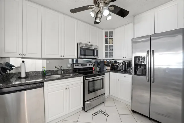 a kitchen with granite countertop a refrigerator a sink and white cabinets
