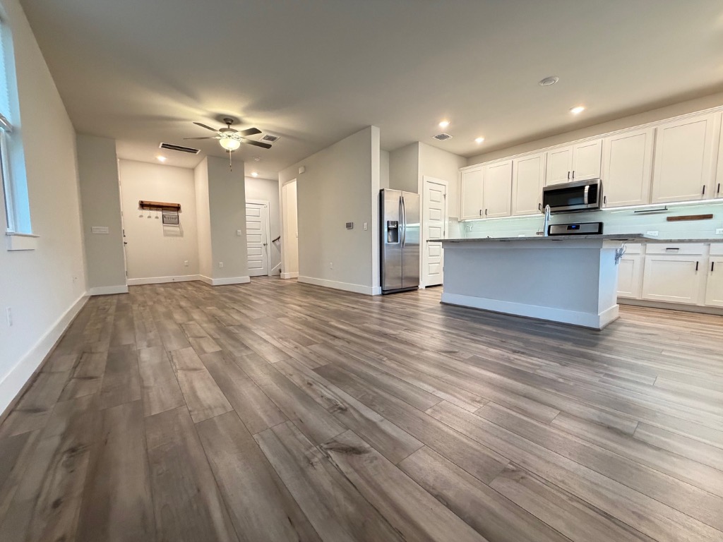7417 Acela Trail, Unit 231 Austin, TX 78744 - Photo 14 of 15 Kitchen featuring open floor plan, white cabinets, a center island with sink, stainless steel appliances, and dark wood finished floors