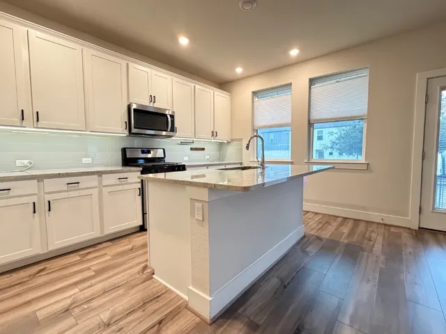 a kitchen with stainless steel appliances granite countertop white cabinets a sink a stove a refrigerator and microwave with wooden floor