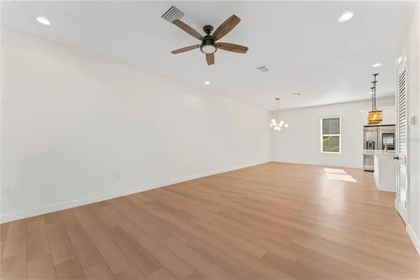 an empty room with wooden floor a ceiling fan and kitchen view