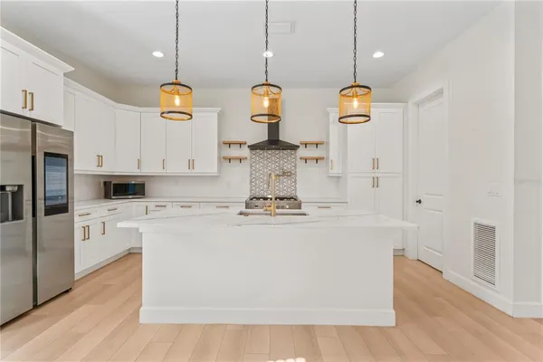 a kitchen with stainless steel appliances granite countertop a sink a stove a refrigerator and white cabinets with wooden floor