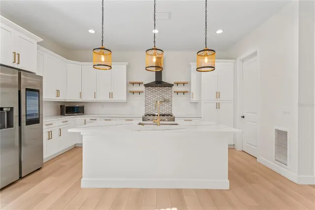 a kitchen with stainless steel appliances granite countertop a sink a stove a refrigerator and white cabinets with wooden floor