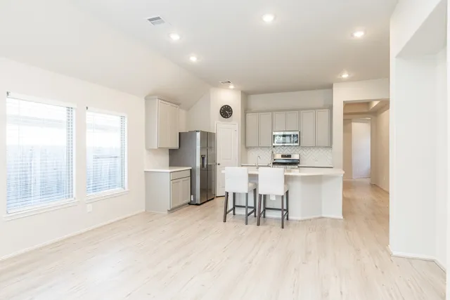 a kitchen with stainless steel appliances a refrigerator a stove a sink dishwasher and a dining table with wooden floor