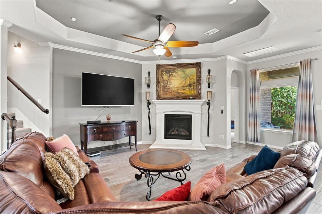3908 Ranchman Boulevard Denton, TX 76210 - Photo 7 of 29 Living area with wood-finish tile flooring, a fireplace with a white mantel, and a tray ceiling with a ceiling fan