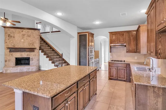 a view of a kitchen with stainless steel appliances granite countertop a stove top oven a sink dishwasher a refrigerator and a dining table with wooden floor