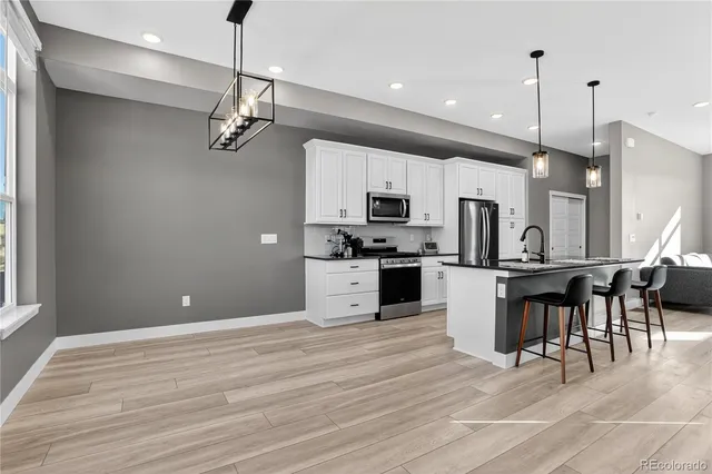 a kitchen with stainless steel appliances kitchen island granite countertop a refrigerator a stove top oven a sink dishwasher and a dining table with wooden floor