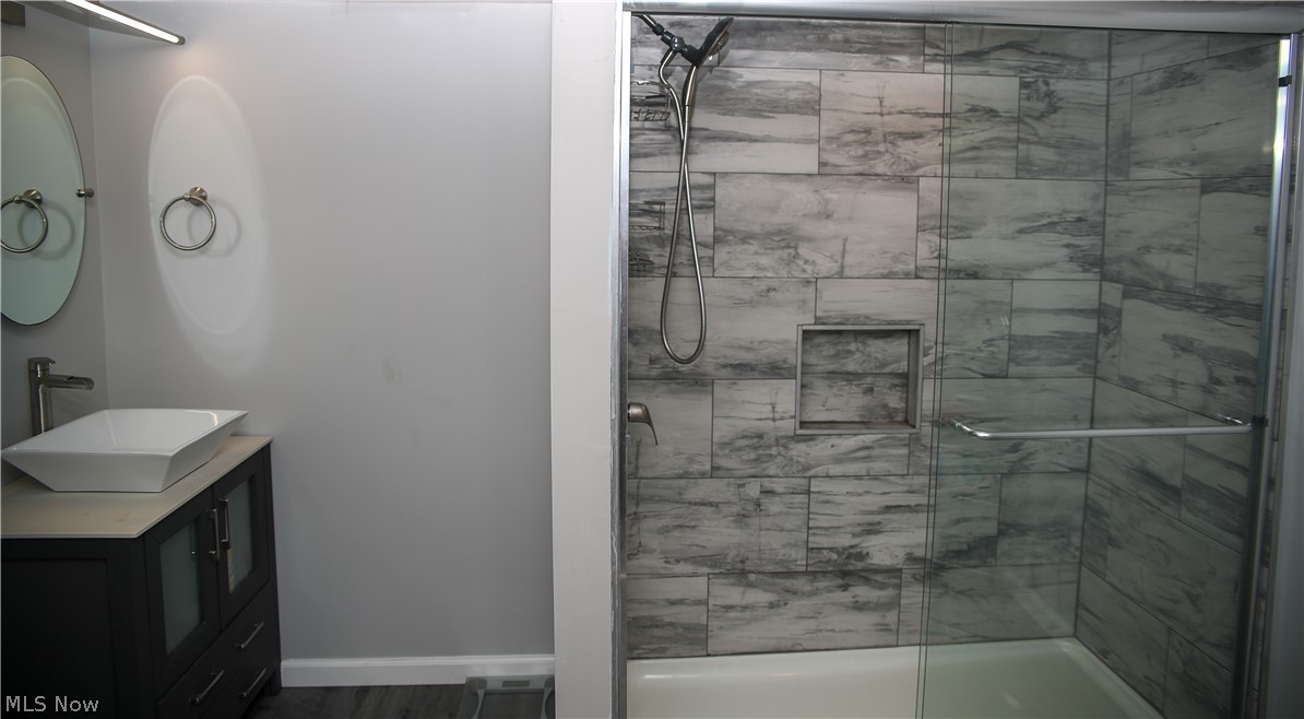 1087 Krumroy Road Akron, OH 44306 - Photo 17 of 23 Modern bathroom featuring a glass-enclosed shower with tile surround and built-in niche, a white vessel sink atop a dark vanity, and an oval wall mirror