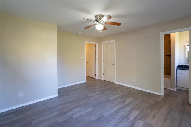 an empty room with wooden floor fan and windows