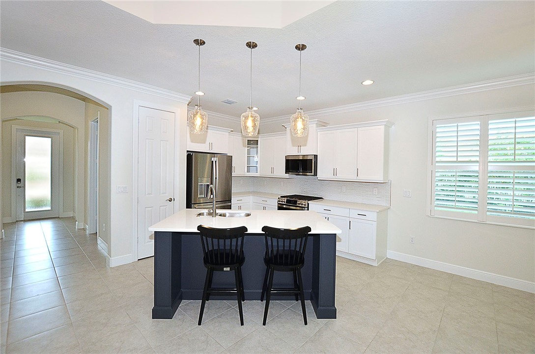 6145 Bella Rosa Lane Vero Beach, FL 32966 - Photo 9 of 36 a kitchen with stainless steel appliances kitchen island granite countertop a sink a stove a dining table and chairs