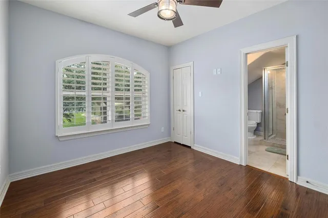 an empty room with wooden floor chandelier fan and windows