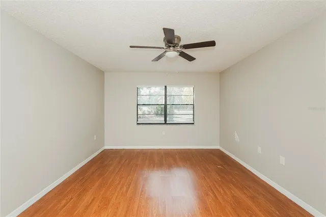 an empty room with wooden floor ceiling fan and windows