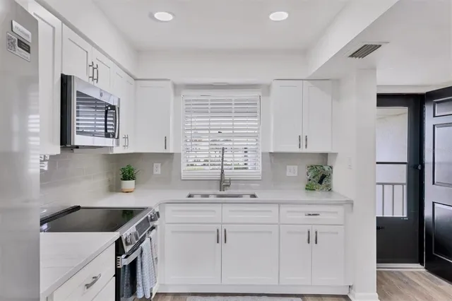 a kitchen with granite countertop a sink cabinets stainless steel appliances and a window
