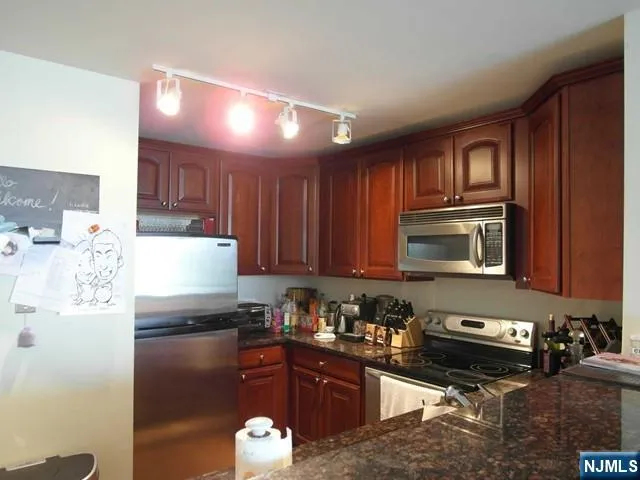 a kitchen with stainless steel appliances granite countertop a refrigerator a stove top oven and a sink with wooden cabinets