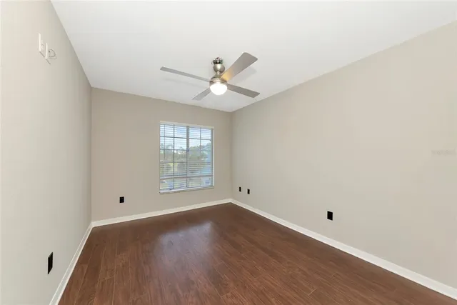 an empty room with wooden floor fan and windows
