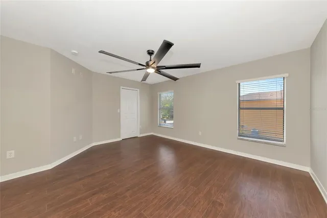 a view of an empty room with wooden floor and a ceiling fan