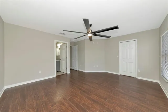 a view of an empty room with wooden floor and a ceiling fan