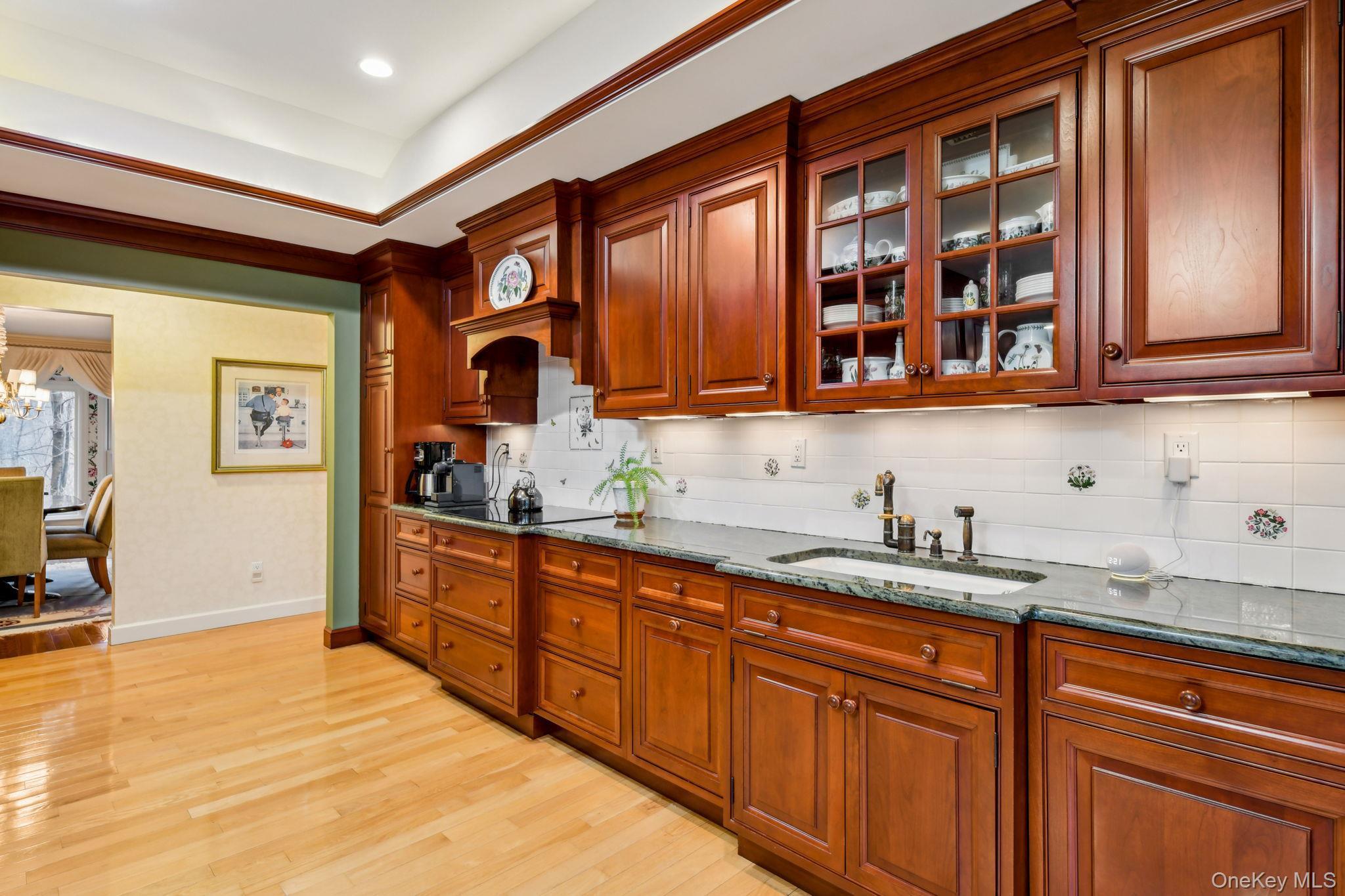 7 Short Path St. James, NY 11780 - Photo 2 of 17 Kitchen featuring dark stone counters, glass insert cabinets, decorative backsplash, light wood-type flooring, and brown cabinets