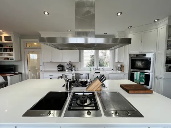 a kitchen with stainless steel appliances a sink a stove a microwave a refrigerator a stove and white cabinets with wooden floor