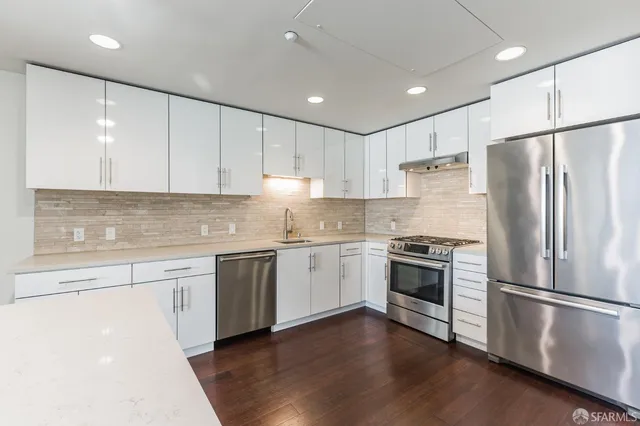a kitchen with granite countertop stainless steel appliances a refrigerator a sink and white cabinets