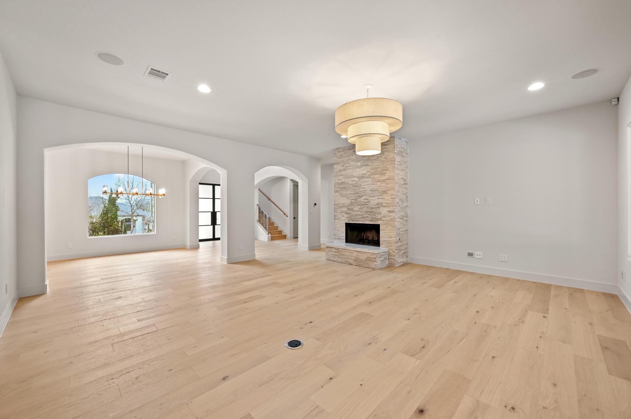 2800 Barton Point Drive Austin, TX 78733 - Photo 7 of 40 Unfurnished living room with arched walkways, a stone fireplace, light wood finished floors, and a chandelier
