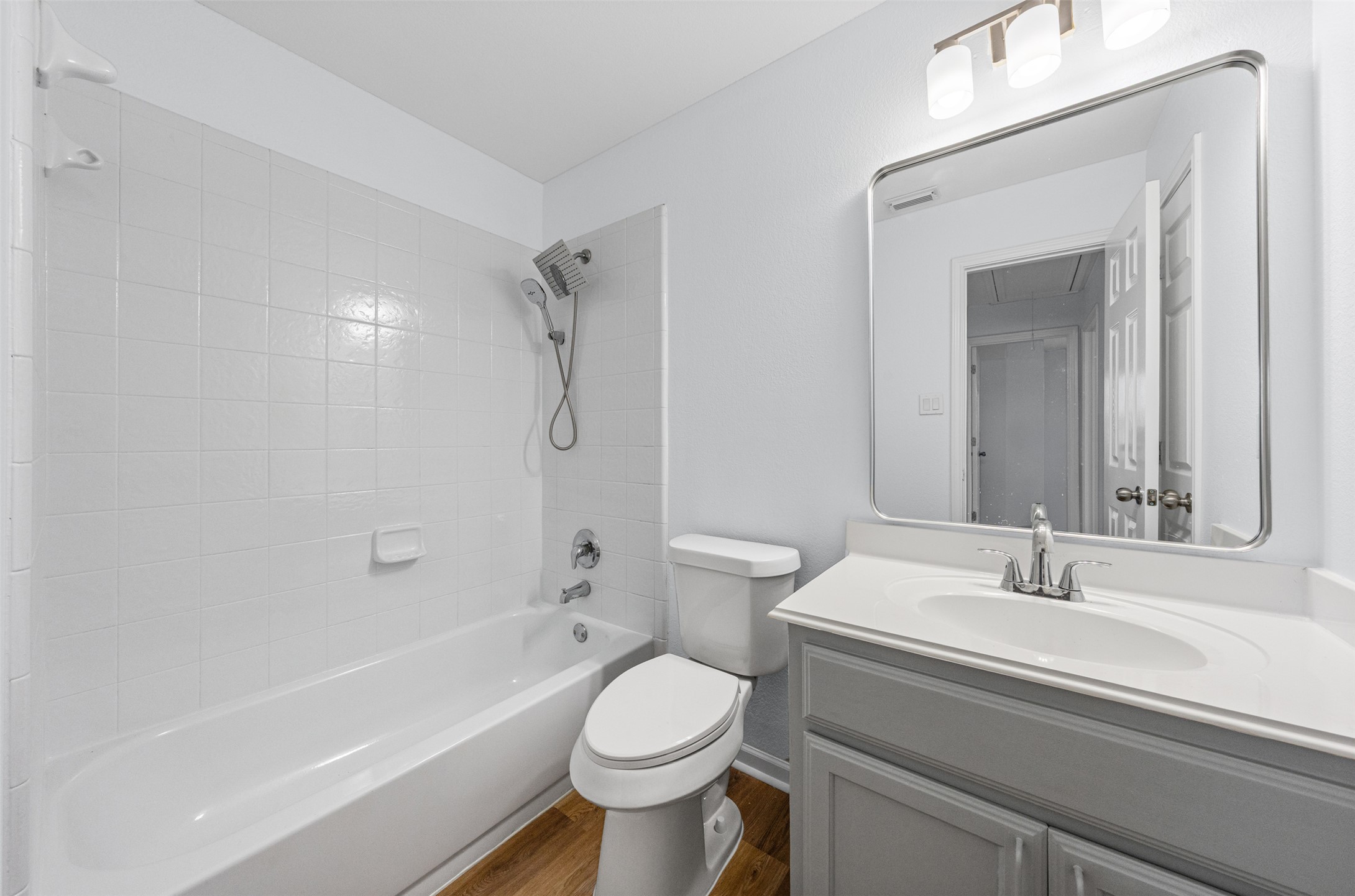 243 Engineers Pass Jarrell, TX 76537 - Photo 22 of 40 Bathroom featuring a white subway tile shower surround with a rainfall showerhead, a white bathtub, and a wood-finish flooring