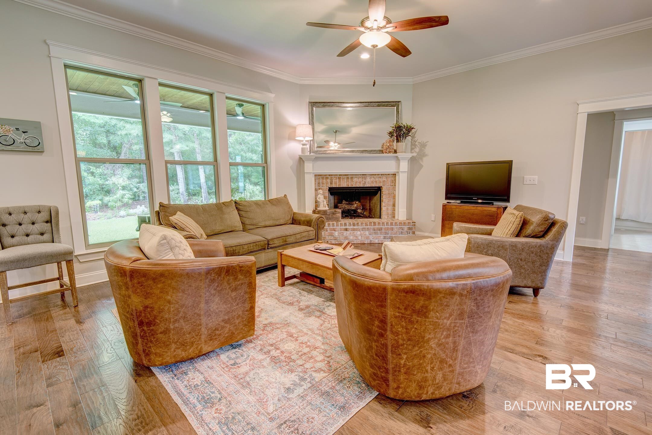 18754 Treasure Oaks Road Gulf Shores, AL 36542 - Photo 12 of 53 Living area featuring wood-finish flooring, a ceiling fan, a brick fireplace with a white mantle, and multiple large windows