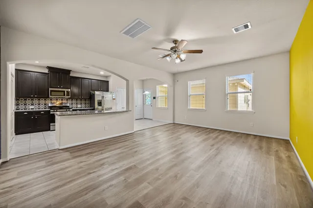 a view of an empty room with kitchen and window