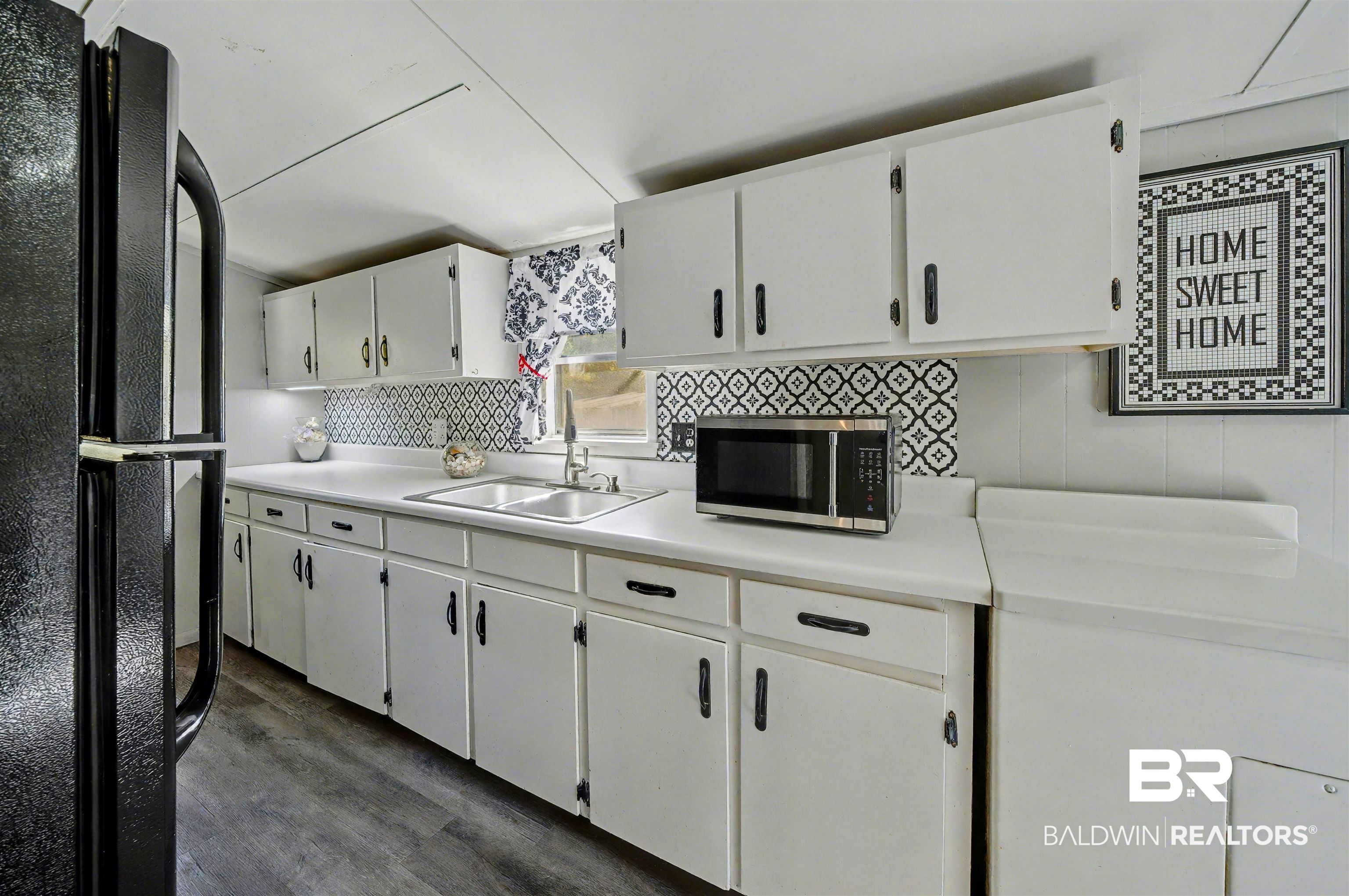 209 West Magnolia Avenue Foley, AL 36535 - Photo 19 of 23 Kitchen featuring freestanding refrigerator, light countertops, white cabinets, dark wood-style floors, and stainless steel microwave