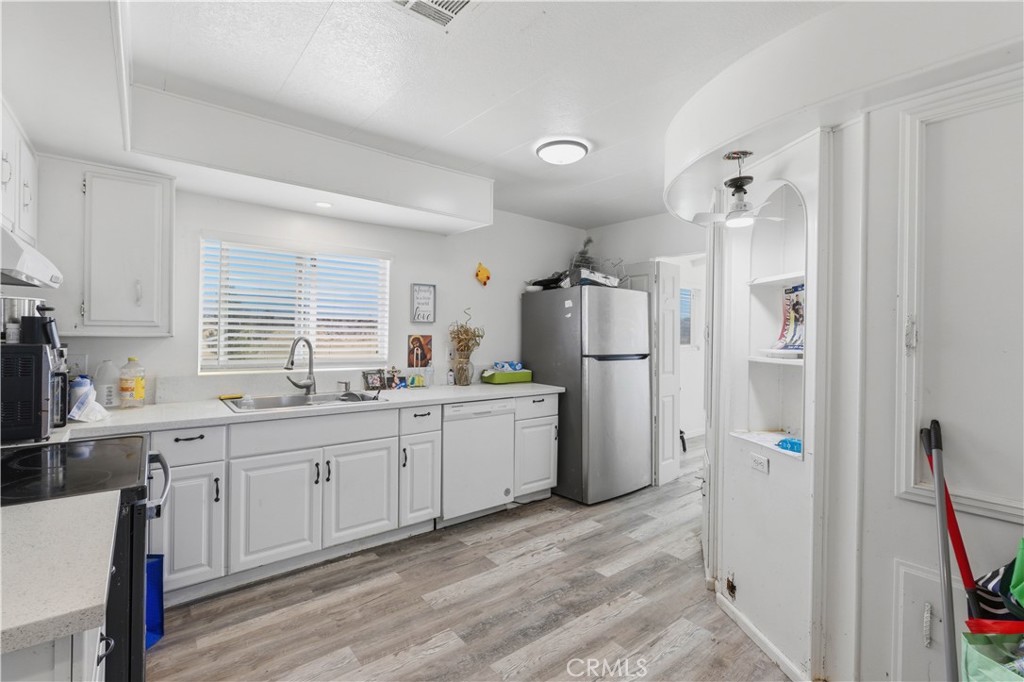 5885 Dos Palmas Road Phelan, CA 92371 - Photo 9 of 40 a large white kitchen with a refrigerator a sink dishwasher a stove and a dining table with wooden floor