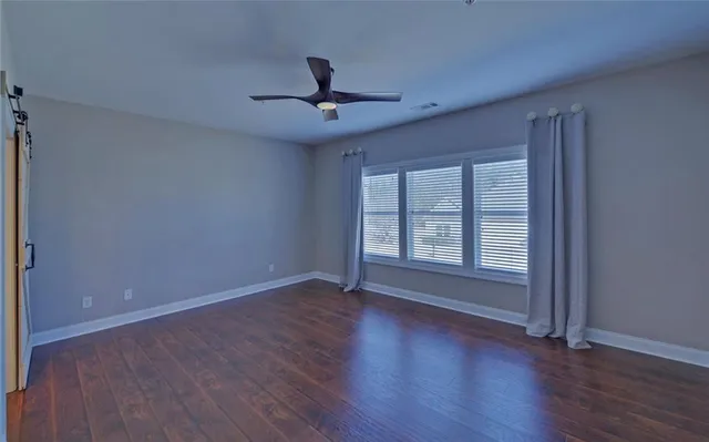an empty room with wooden floor fan and windows