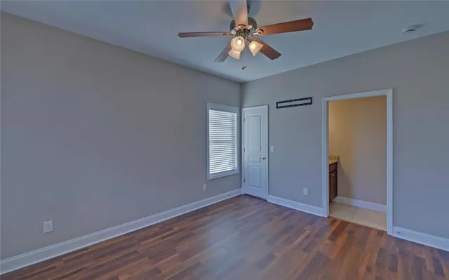 a view of an empty room with wooden floor and a ceiling fan