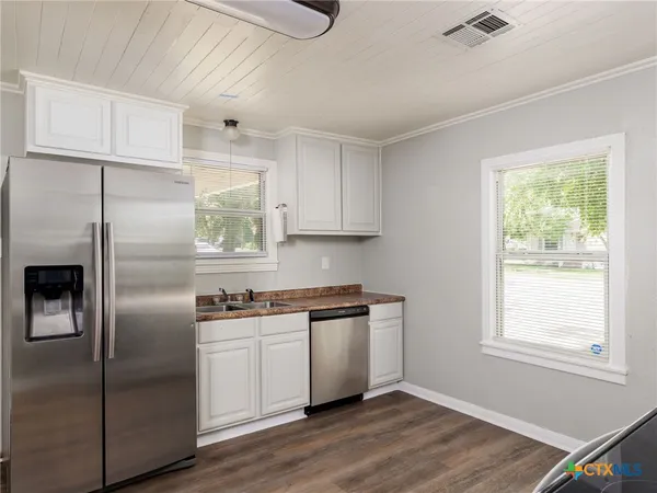 a kitchen with stainless steel appliances granite countertop a refrigerator a sink a stove and white cabinets with wooden floor