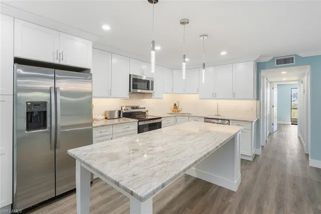 a large kitchen with kitchen island a large counter top stainless steel appliances and wooden floor