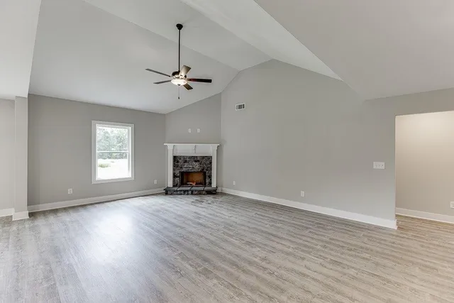 an empty room with wooden floor ceiling fan and windows